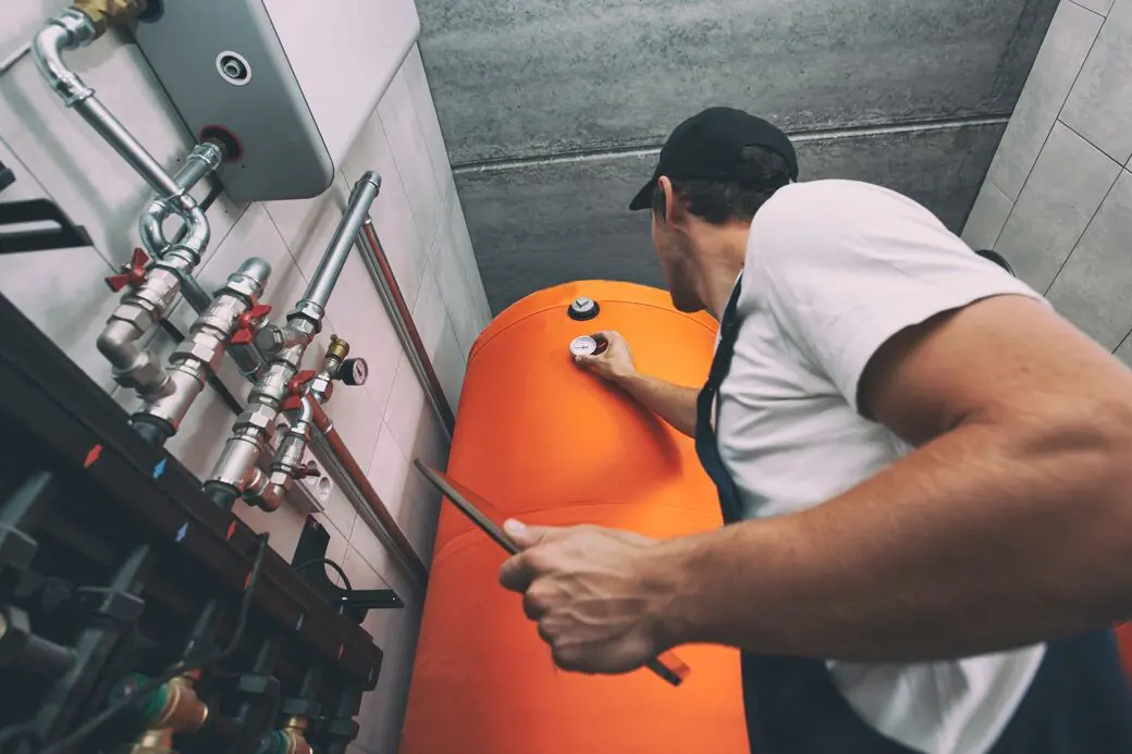 Monteur prüft mit Werkzeug in der Hand die Anschlüsse an einer Heizungsanlage im Technikraum.